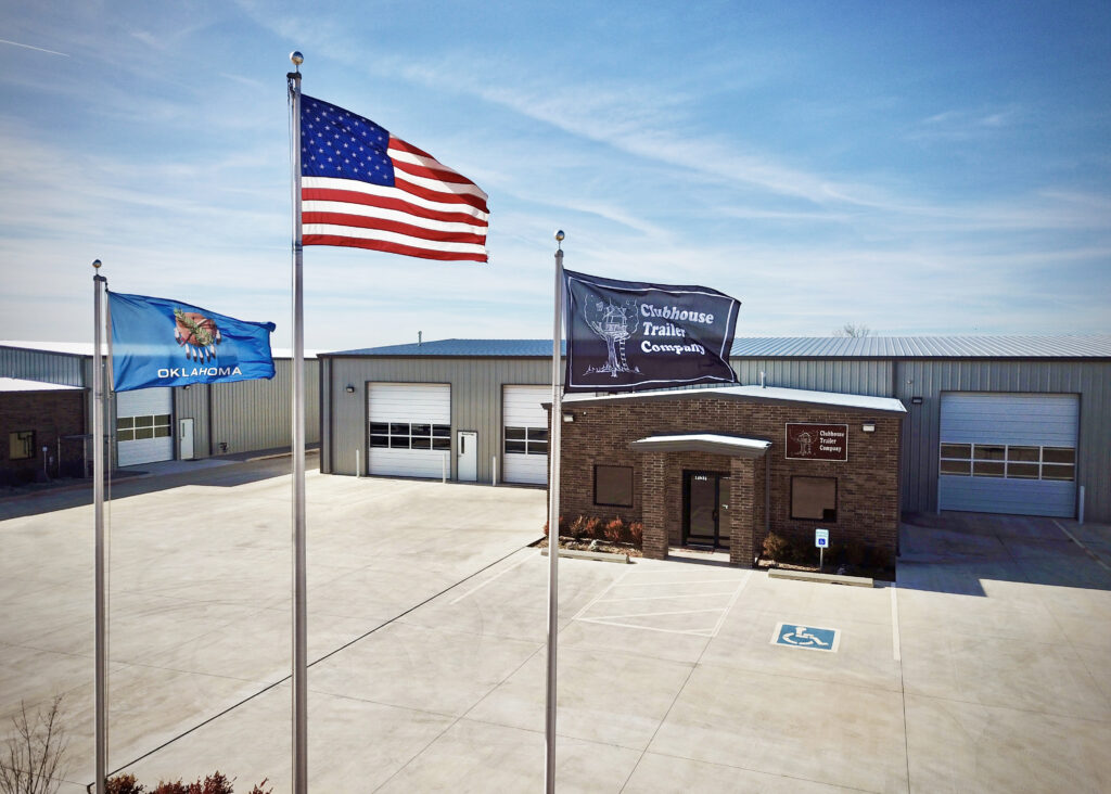 The American, Oklahoma, and Clubhouse Trailer Company flags flying outside of the shop