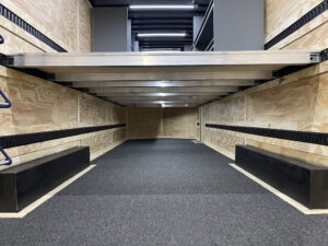 Underneath the second floor in a small trailer solution, completed with interior lighting, instrument shelving, and a drum wall.